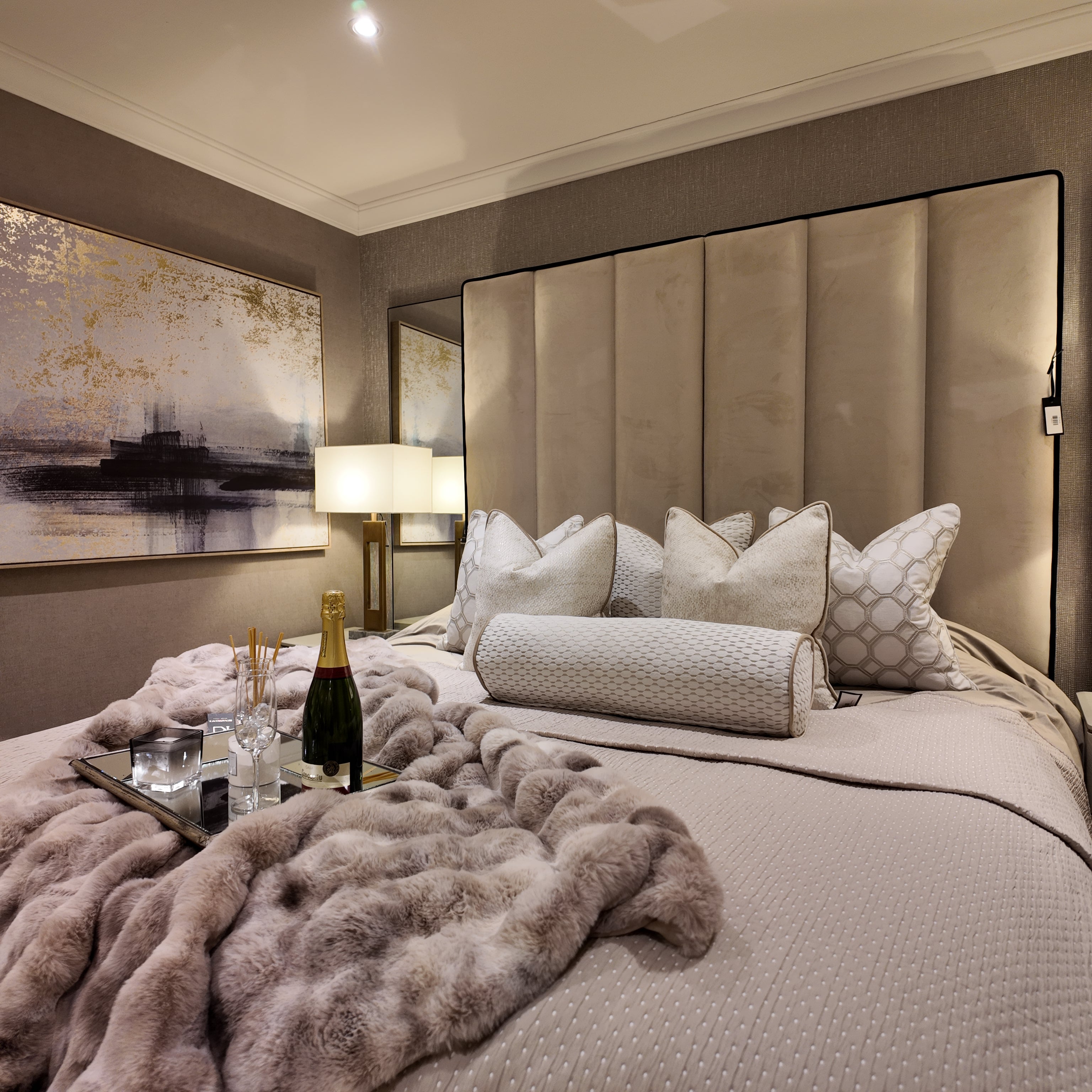 Luxurious bedroom with a large bed, decorative pillows, and a tray with wine and glasses.